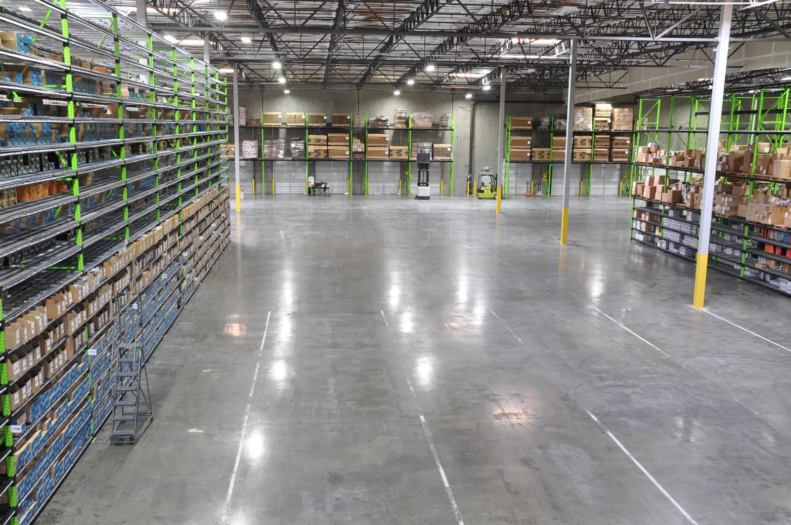 Wide warehouse floor bordered by tall green storage racks